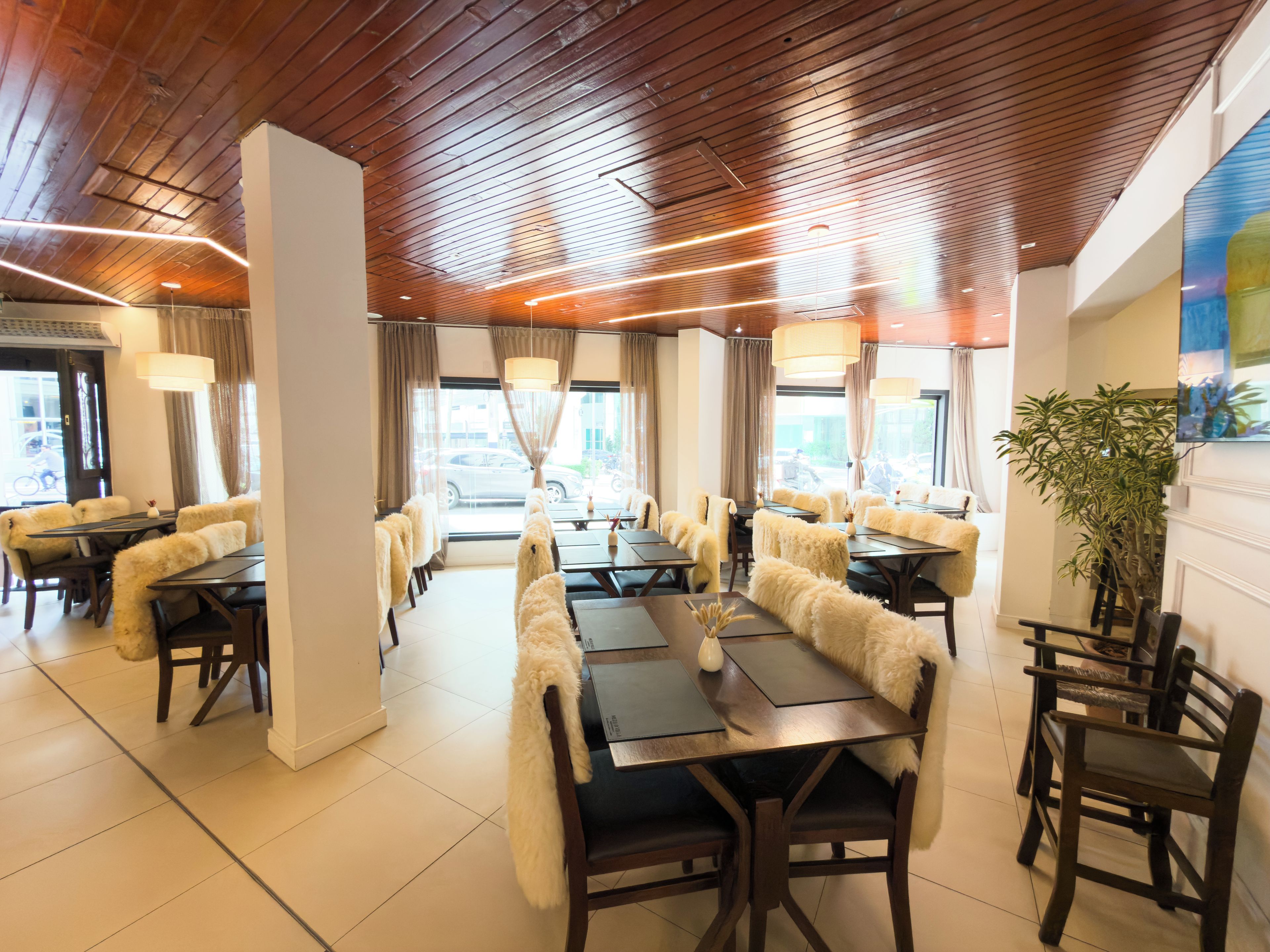 A restaurant with wooden ceiling, multiple tables, and chairs.
