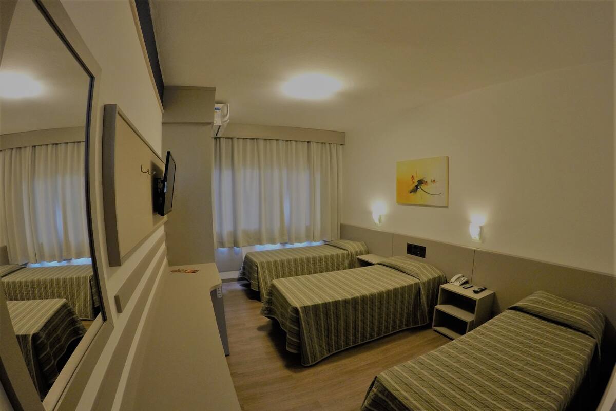 Ein Hotelzimmer mit zwei Einzelbetten, einem Schreibtisch, einem Stuhl, einem Telefon und einem Bild an der Wand.