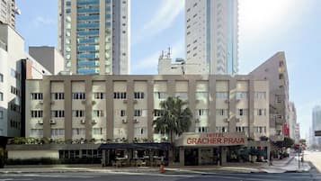Um hotel com vários andares, restaurante visível e uma palmeira na frente.