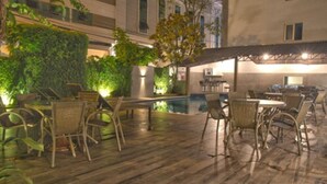 An outdoor patio area with wooden flooring, wicker furniture, and a pool. - Hotel Gracher Praia (Balneário Camboriú)