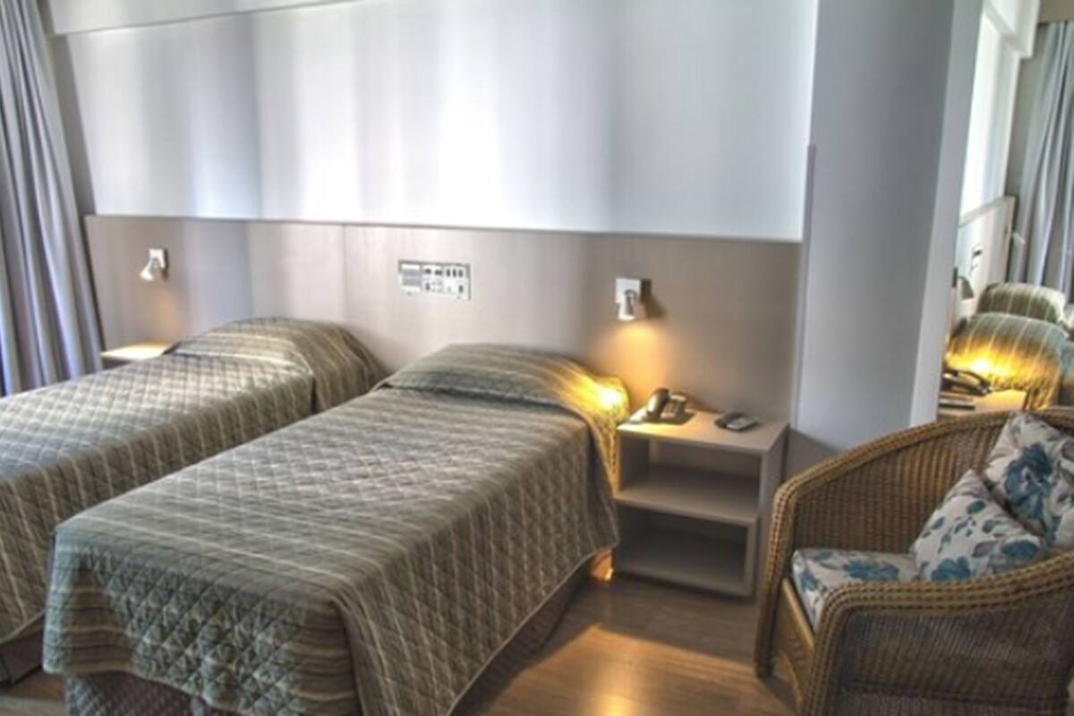 Ein Hotelzimmer mit zwei Betten, einem Nachttisch, einem Stuhl und einer an der Wand befestigten Bedieneinheit.
