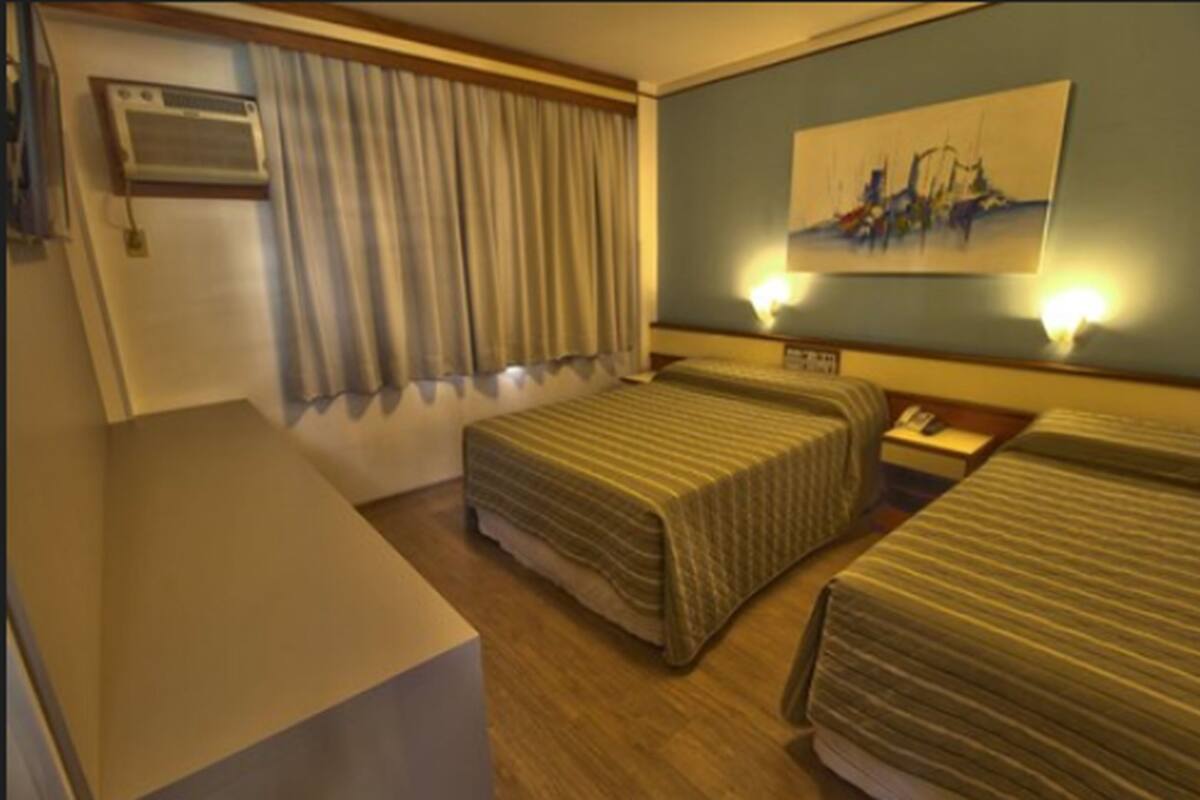 Ein Hotelzimmer mit zwei Betten, einem Schreibtisch, einer Klimaanlage und einem Bild an der Wand.