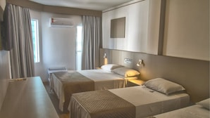 A hotel room with two single beds, a desk, a chair, an air conditioning unit, and a wall-mounted TV.