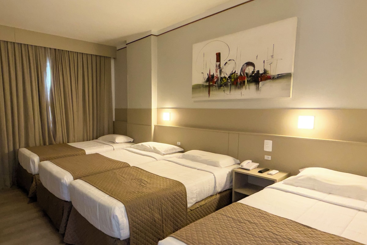 Une chambre d’hôtel avec deux lits, une table de chevet, un tableau au mur et une fenêtre avec des rideaux.