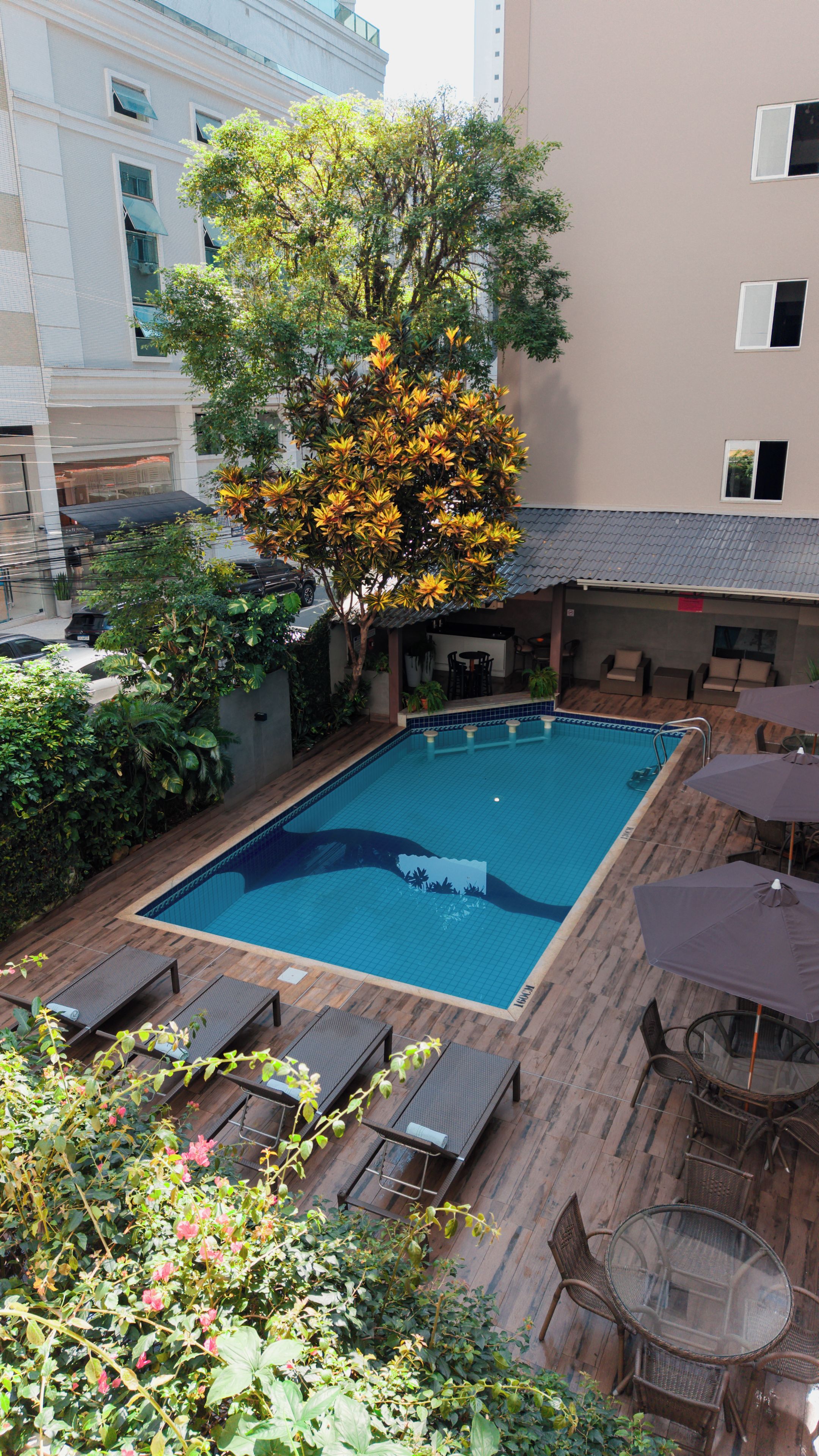 A rectangular swimming pool with a tiled deck, surrounded by lounge chairs and a table with umbrellas.