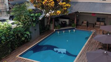 A rectangular swimming pool with a tiled deck, surrounded by lounge chairs and a table with umbrellas.