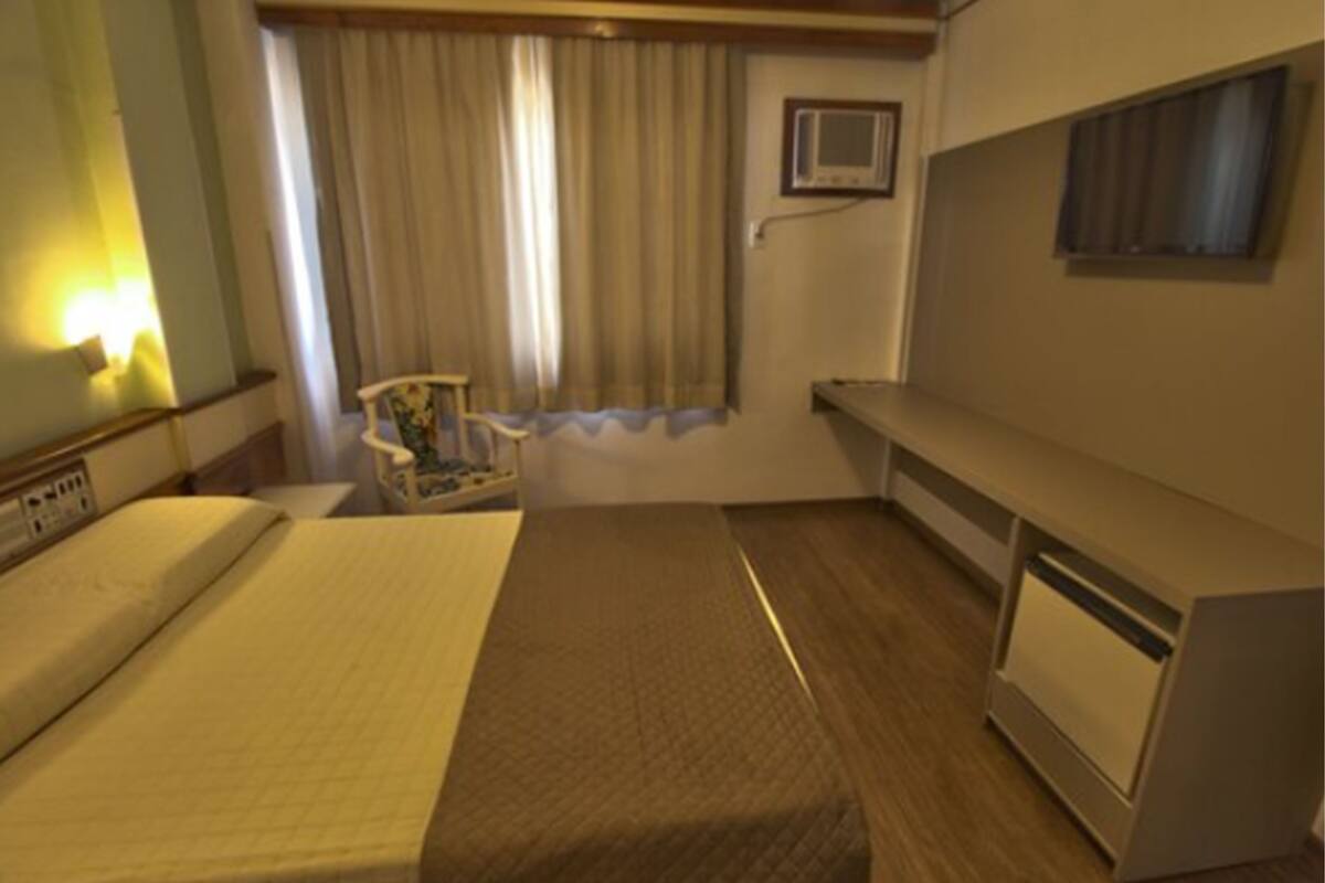 Ein Hotelzimmer mit Bett, Schreibtisch, Stuhl, einem Fenster mit Vorhängen und einem Fernseher.