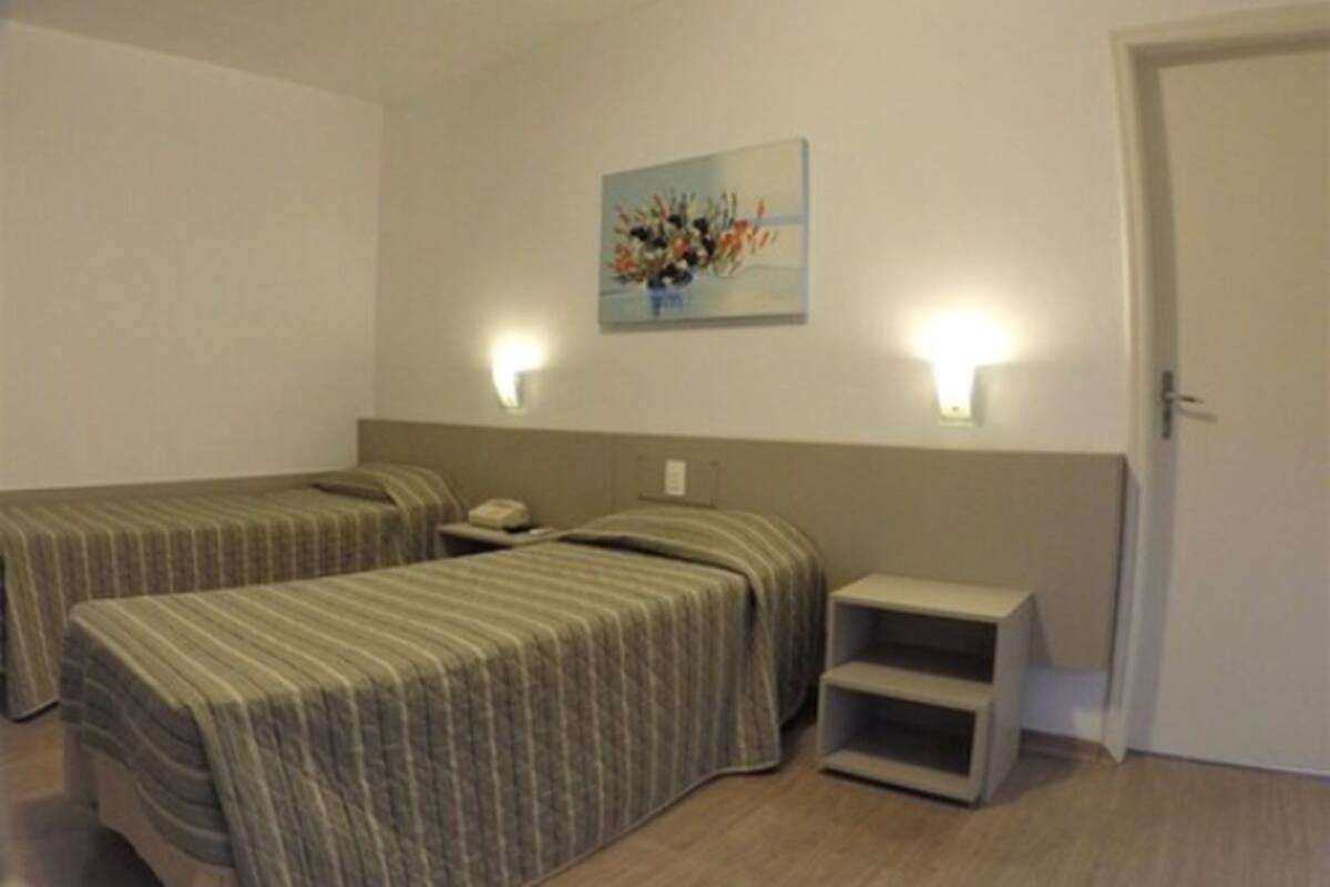 Ein Hotelzimmer mit zwei Einzelbetten, einem Nachttisch mit Lampe, einer kleinen Ablagefläche und einem Bild an der Wand.
