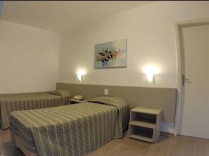 Une chambre d’hôtel avec deux lits simples, une table de chevet avec une lampe, une petite étagère et un tableau au mur.