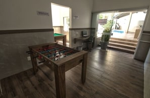 A room with a foosball table, a small pool table, a desk with a computer, and a potted plant. - Hotel Gracher Praia (Balneário Camboriú)