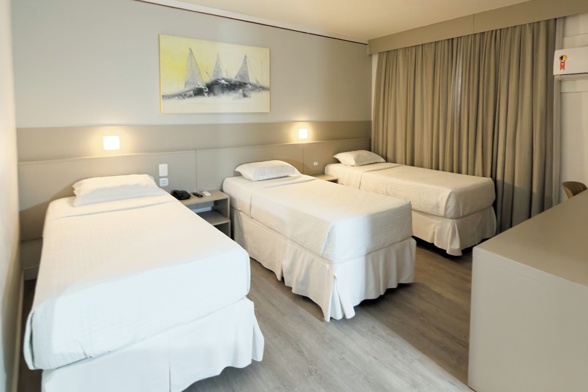 Une chambre d’hôtel avec deux lits simples, un canapé, un tableau au mur et un appareil de climatisation.