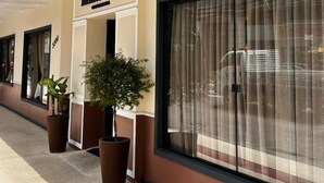 A hotel exterior with a covered walkway, large windows with curtains, and potted plants. - Hotel Gracher Praia (Balneário Camboriú)