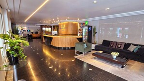 A hotel lobby with a reception desk, seating area, and a refrigerator. - Hotel Gracher Praia (Balneário Camboriú)