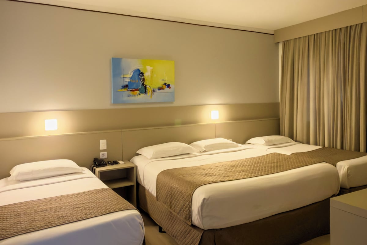 Une chambre d’hôtel avec deux lits, une table de chevet avec une lampe, un tableau au mur et un rideau à la fenêtre.