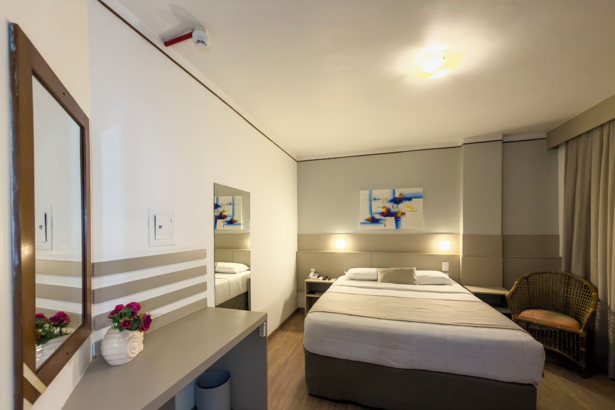 Une chambre d’hôtel avec un lit, une table de chevet, un miroir et une chaise.