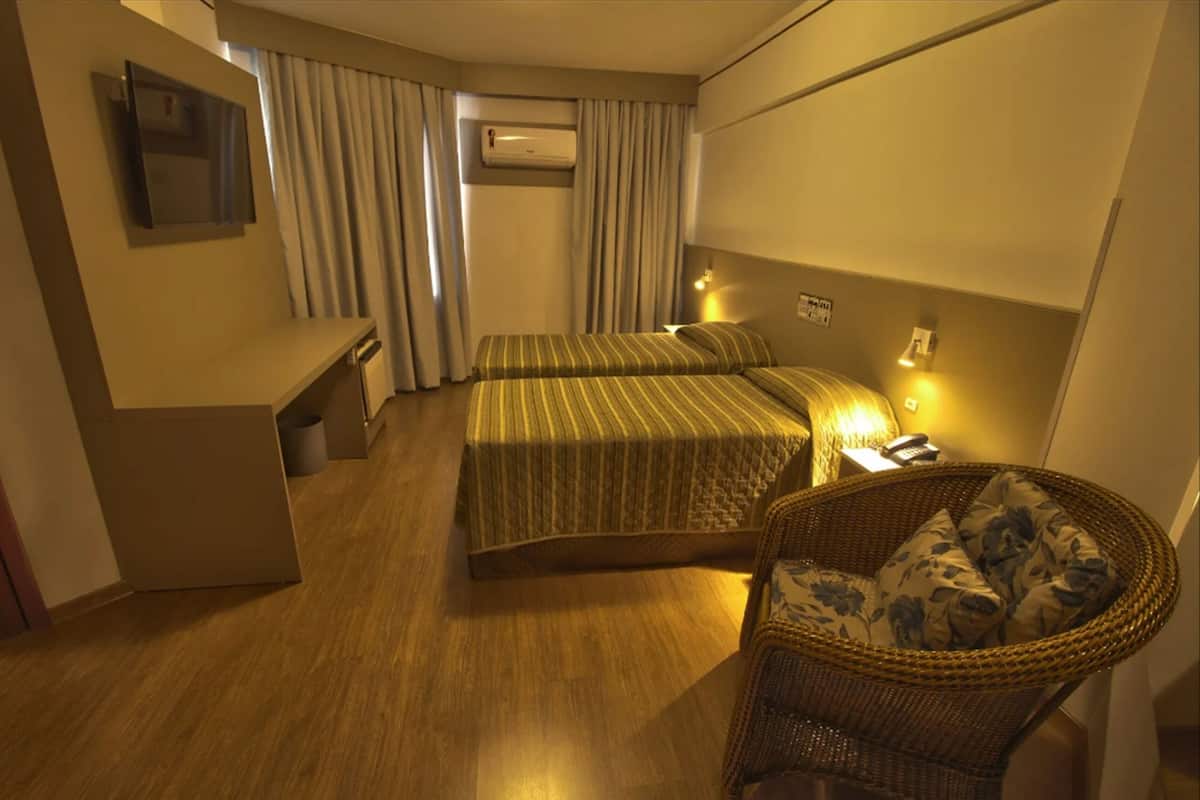 Ein Hotelzimmer mit zwei Betten, einem Schreibtisch, einem Stuhl und einer Klimaanlage.