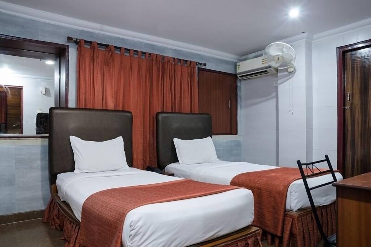 A hotel room with two single beds, a desk, a chair, an air conditioning unit, and a mirror.