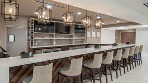 A modern bar area with a long counter, multiple bar stools, and pendant lighting.