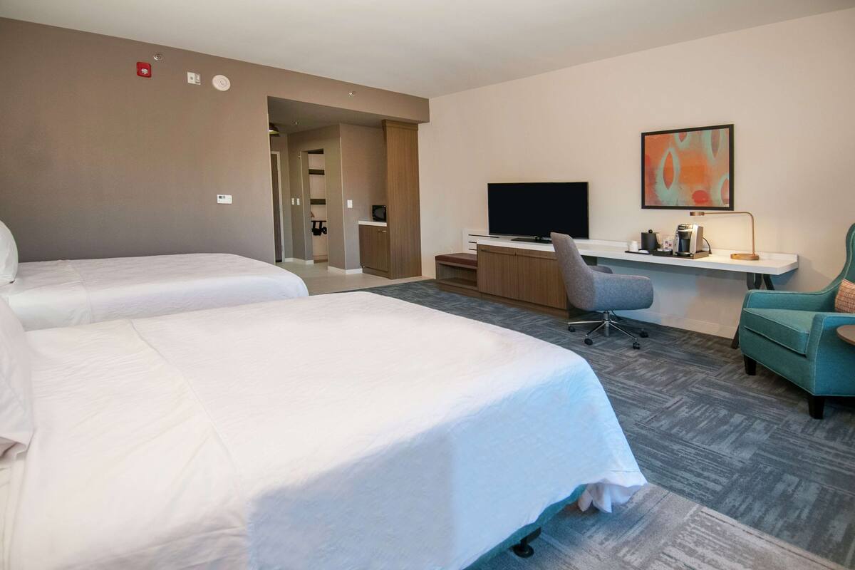 A hotel room with two beds, a desk with a computer, a TV, and a chair.