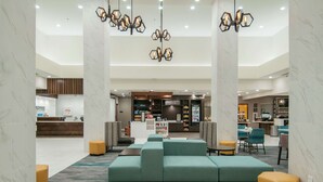 A hotel lobby with a central seating area, a reception desk, and a kitchenette in the background.