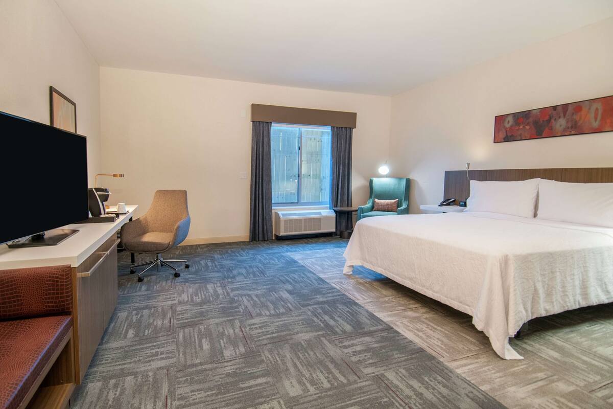 A hotel room with a bed, desk, chair, TV, and a window with curtains.