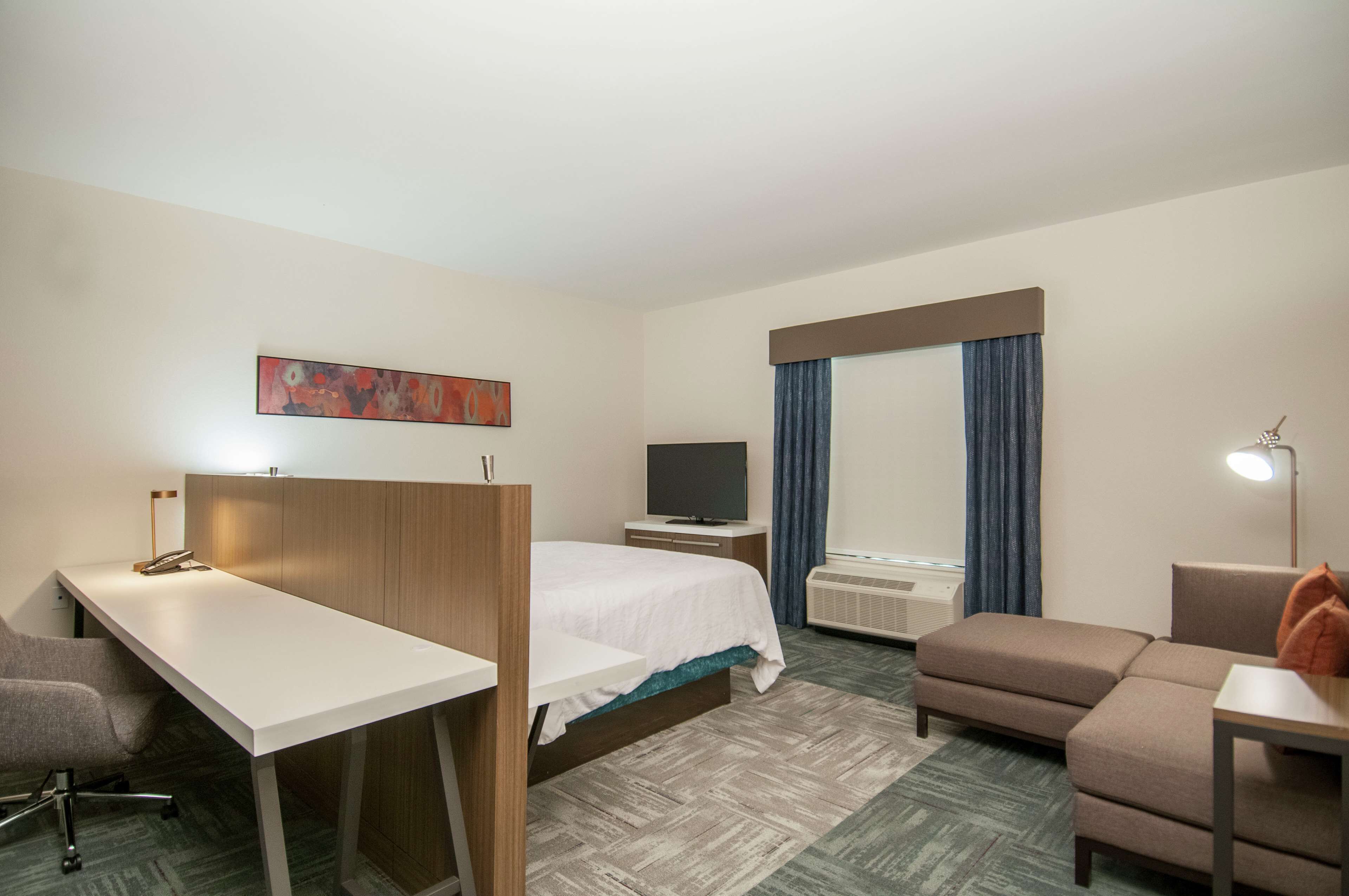 Ein Hotelzimmer mit Bett, Schreibtisch, Stuhl, Fernseher, Lampe und einer Couch.