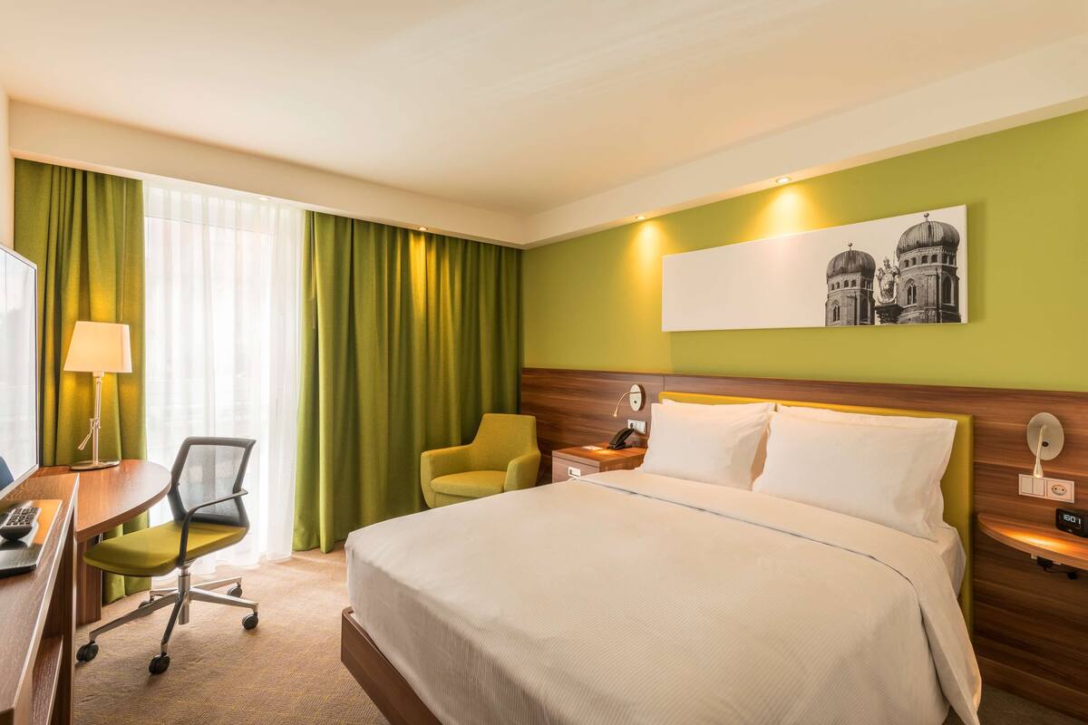 Une chambre d’hôtel avec un lit, un bureau et une chaise, une lampe et un tableau au mur.