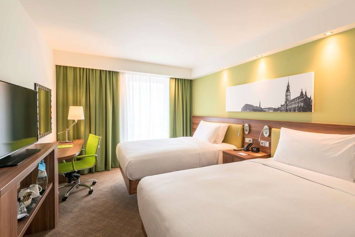 Une chambre d’hôtel avec deux lits, un bureau avec une chaise, une télévision et un tableau au mur.