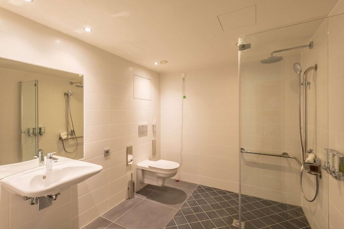 Une salle de bain moderne dotée d’une douche à parois de verre, de toilettes et d’un lavabo.