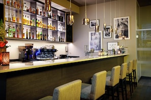 A bar area with a long counter, multiple shelves of bottles, hanging pendant lights, and bar stools.