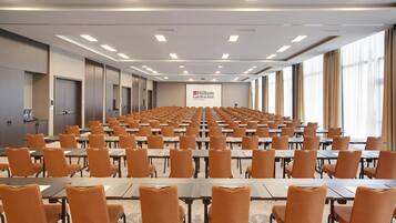 Una grande sala conferenze con file di tavoli e sedie, un podio e il cartello di un Hilton Garden Inn.