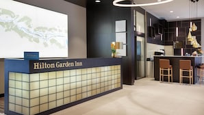 A reception desk with a map projection, a minibar, and a bar area with stools. - Hilton Garden Inn Zurich Limmattal (Spreitenbach)
