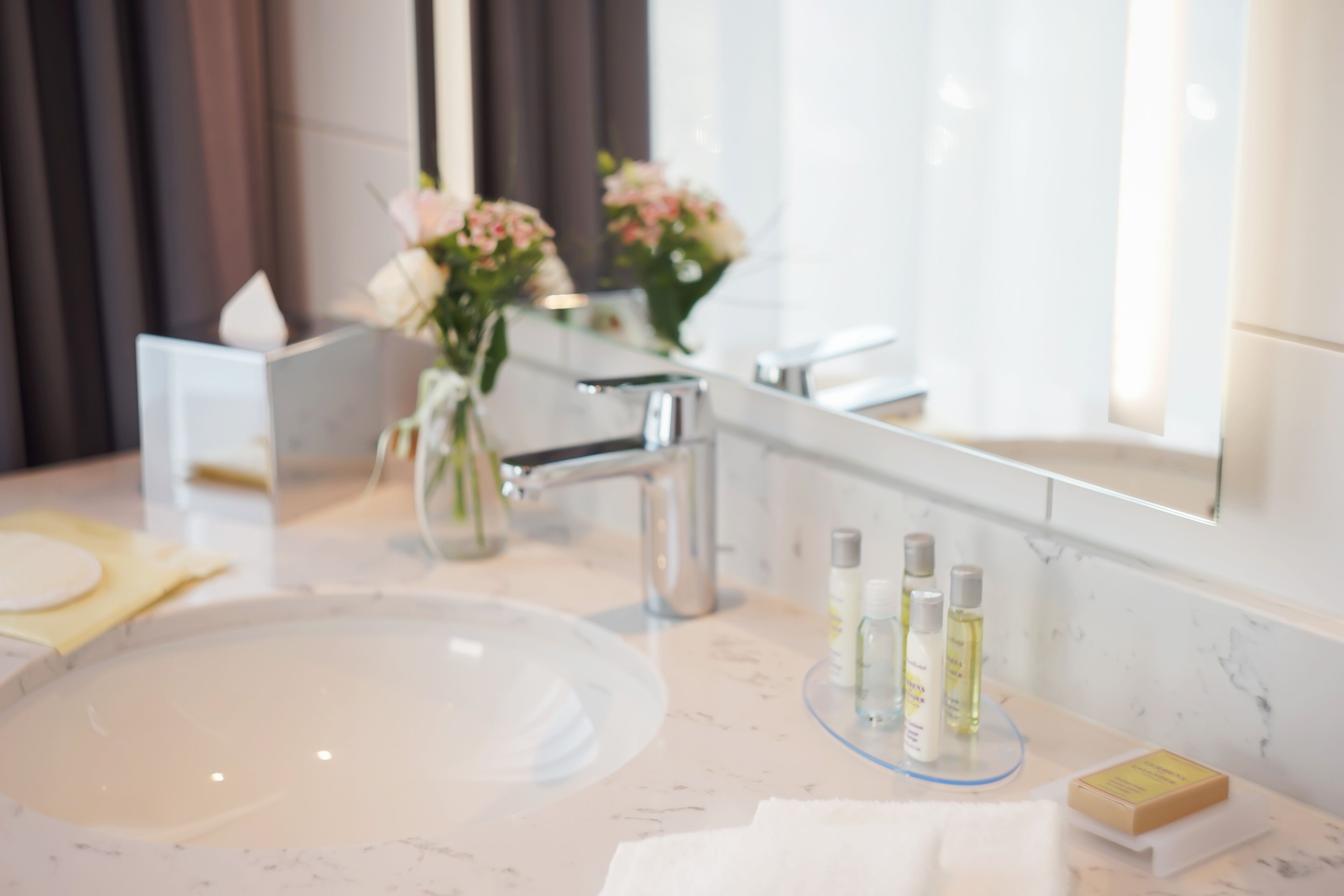 Un baño moderno con lavamanos de mármol, un espejo y un florero con flores.