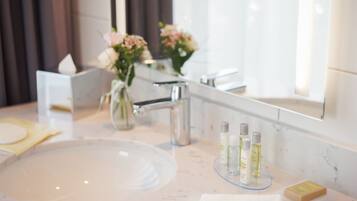 Ein modernes Badezimmer mit Marmorwaschbecken, einem Spiegel und einer Vase mit Blumen.