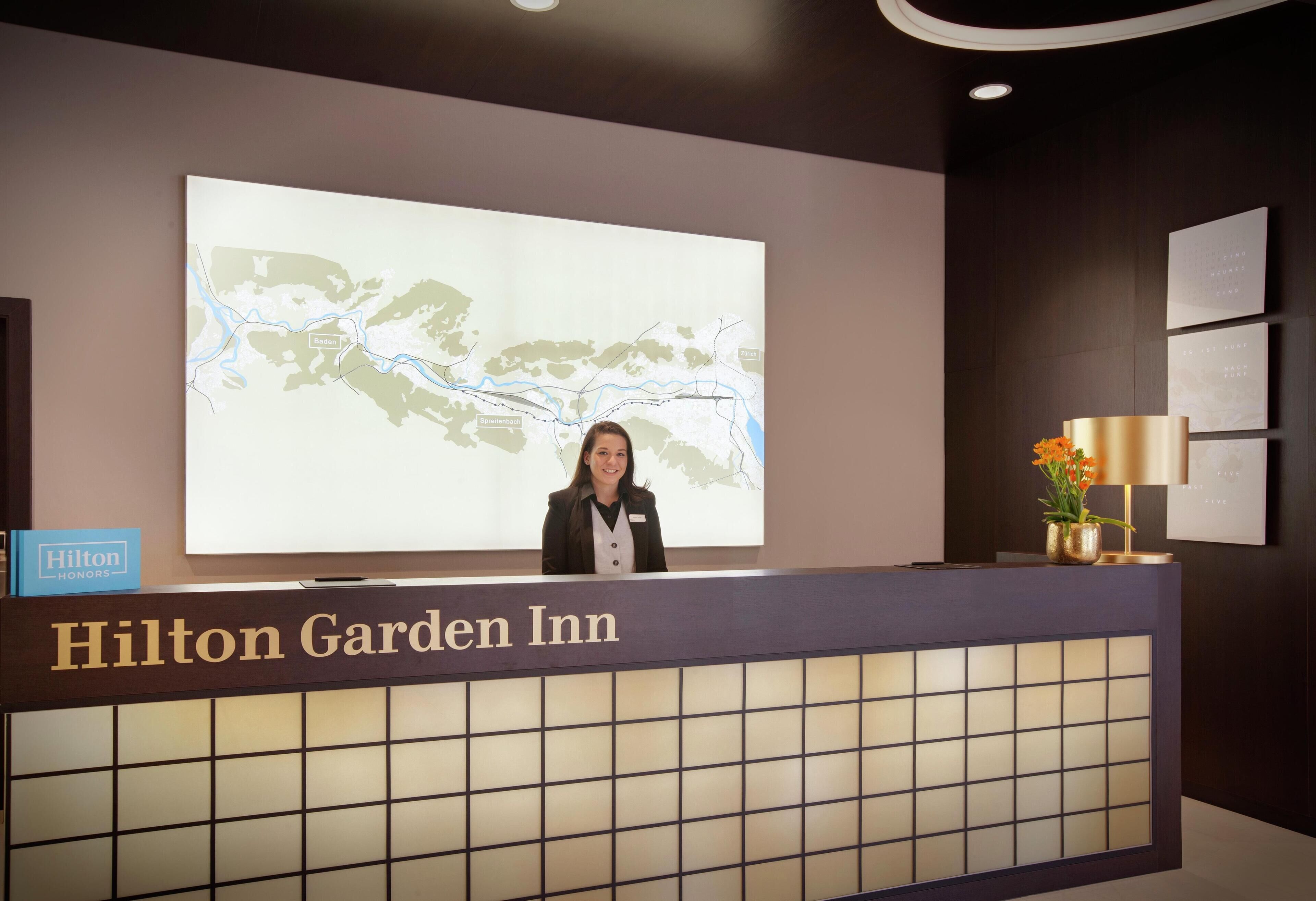 Un comptoir d’accueil dans l’hôtel Hilton Garden Inn, avec une carte affichée et une plaque nominative.