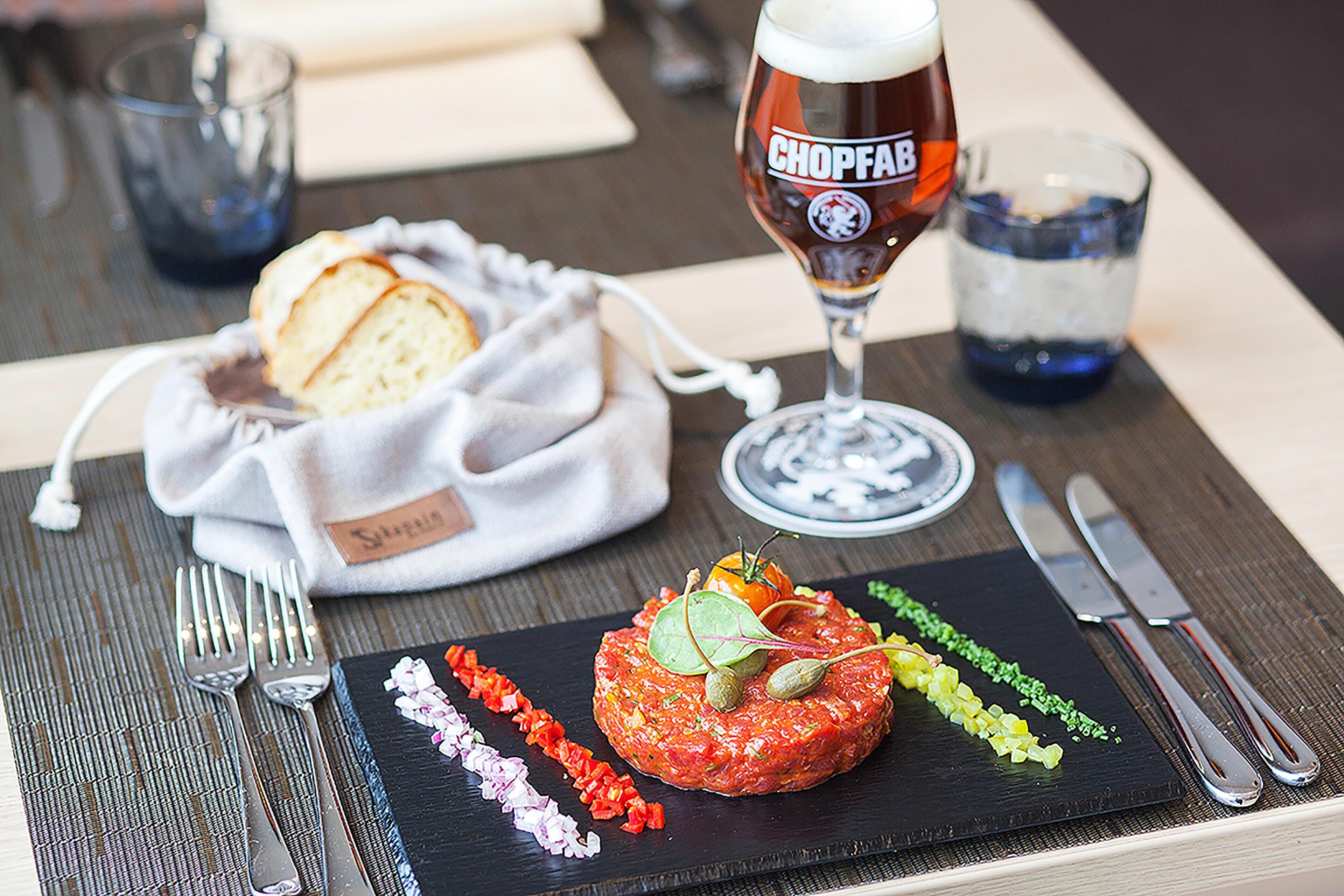 A dining table with a black plate of food, a glass of beer, and a glass of water.