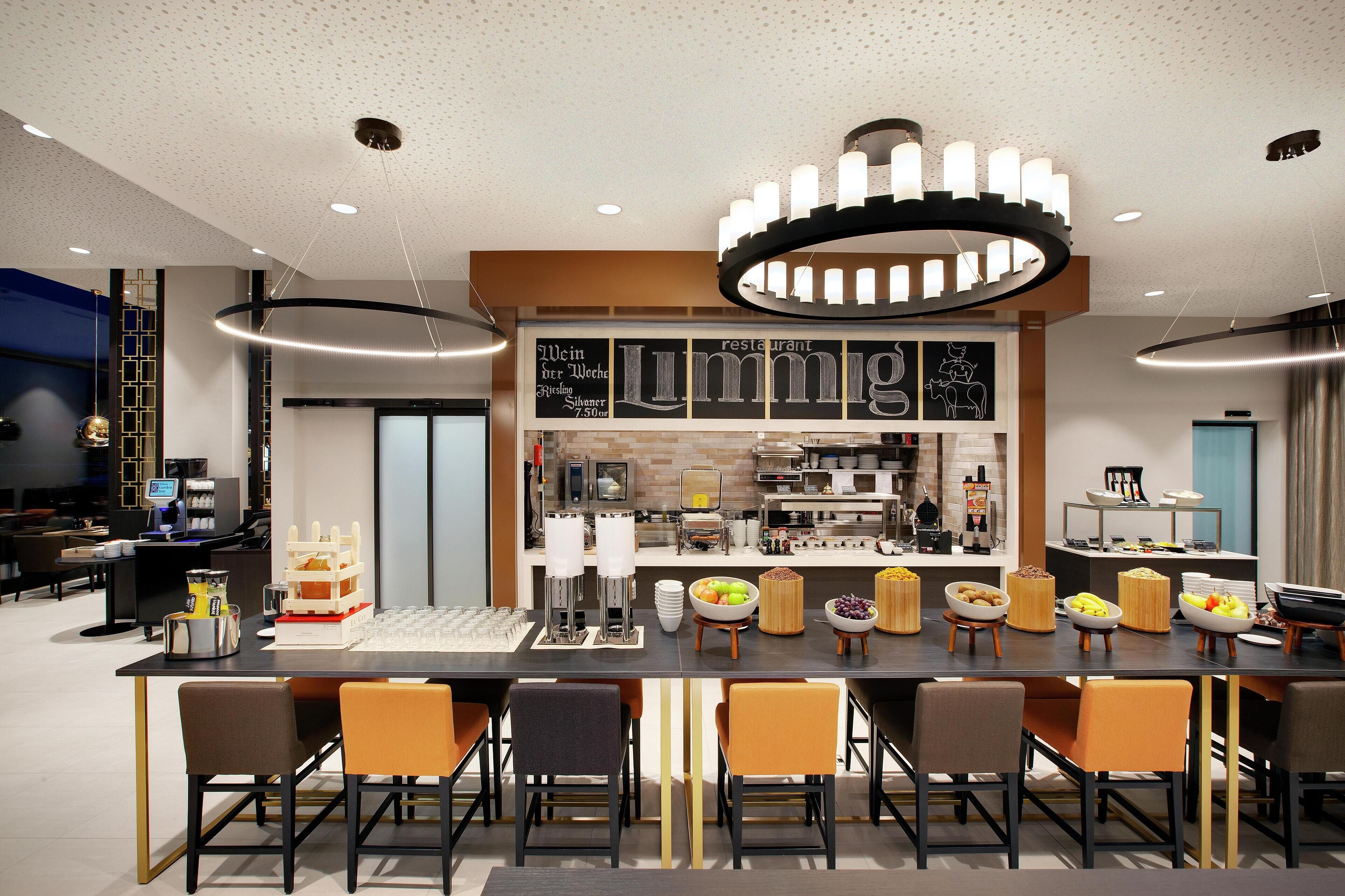 Una barra de desayuno moderna con diversas opciones de comida y bebida, una máquina de café y una pantalla digital que muestra información.