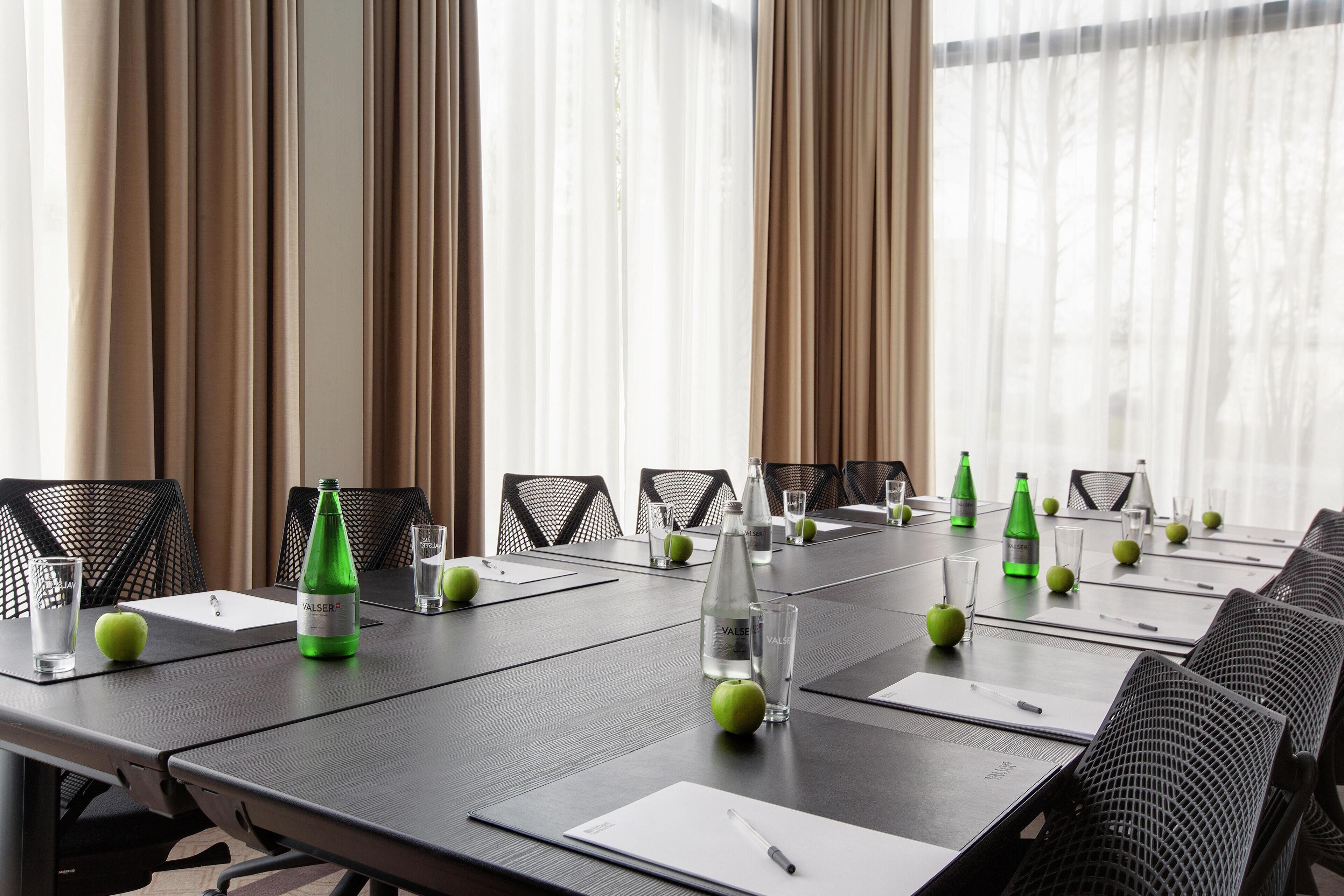 Ein Konferenzraum mit langem Tisch, vorbereitet für Besprechungen, ausgestattet mit Wasserflaschen, Gläsern und Apfelscheiben.
