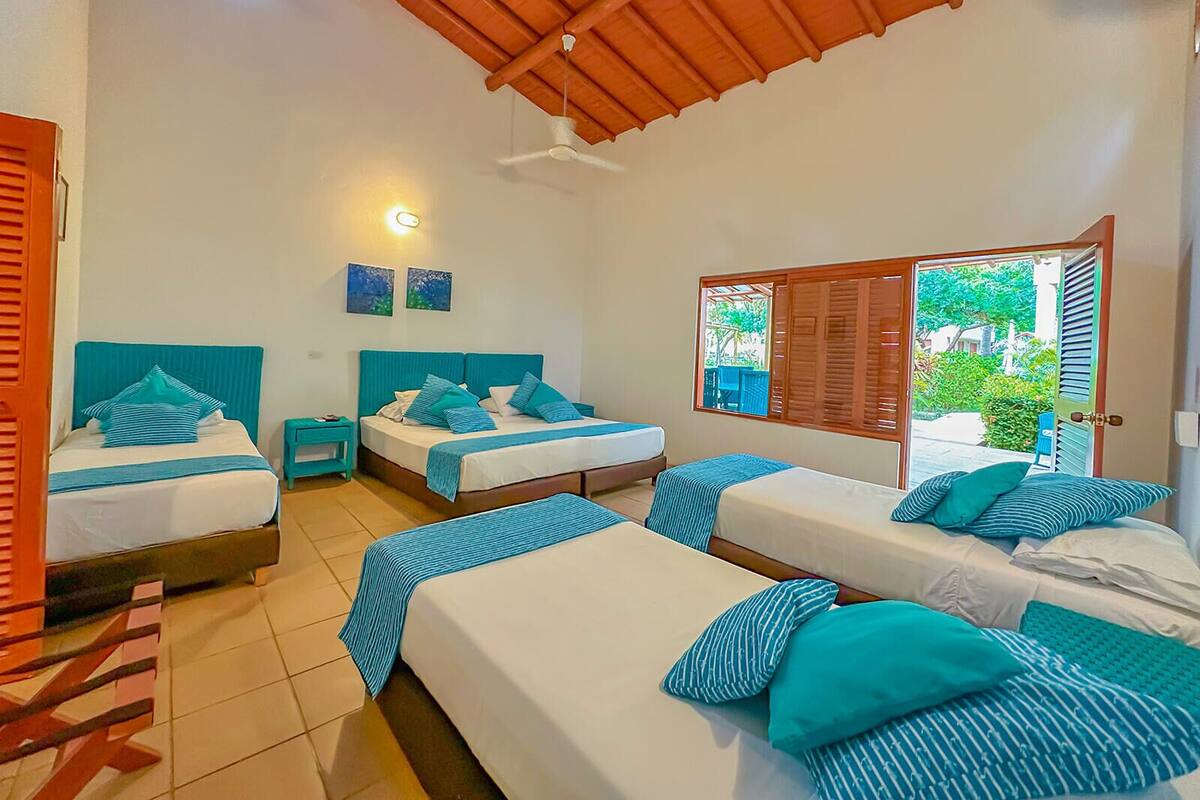 A hotel room with two beds, a ceiling fan, and a window with a view of greenery.