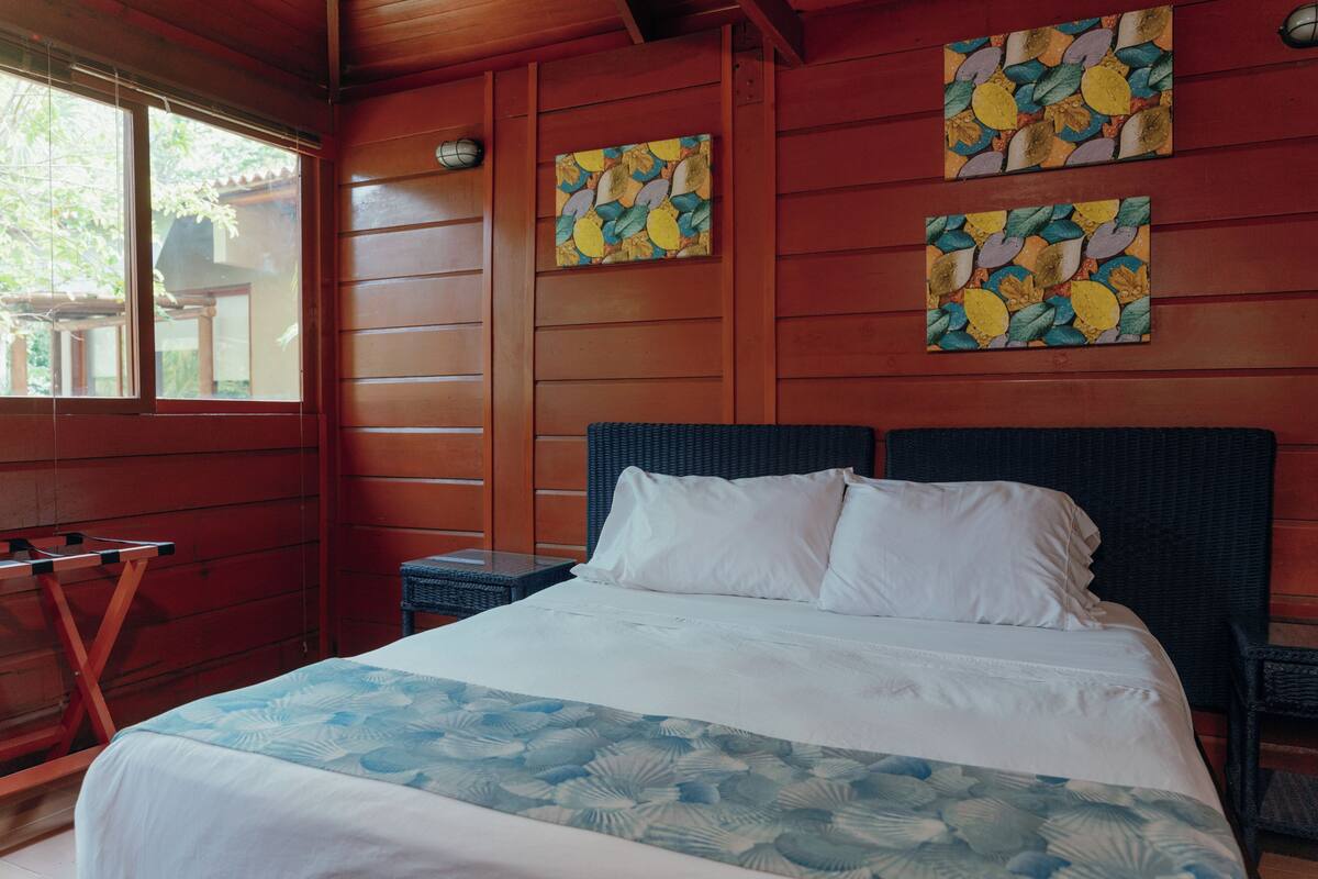 A wooden room with a bed, two wall-mounted artworks, and a window.