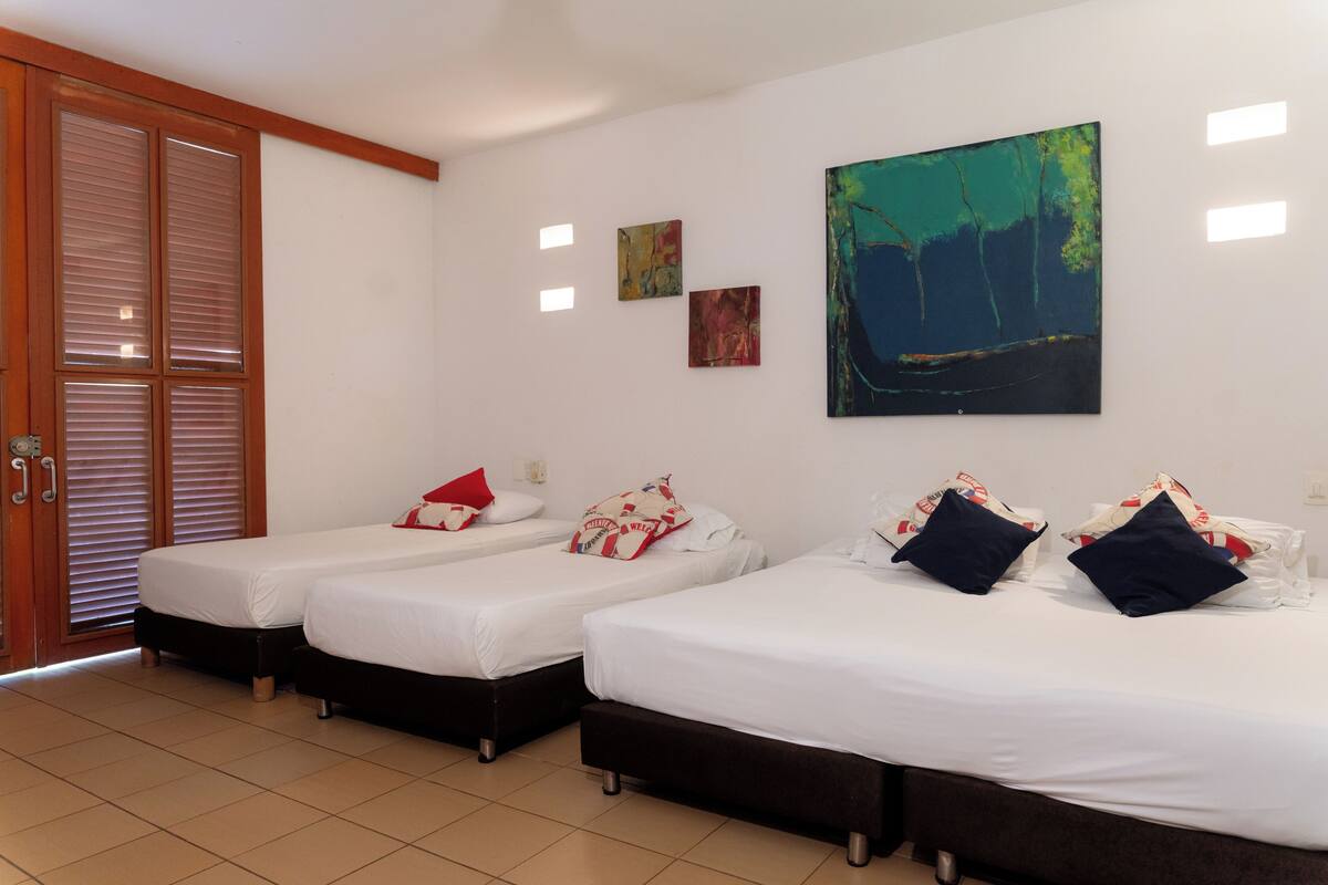 A hotel room with three beds, a large window, and artwork on the wall.