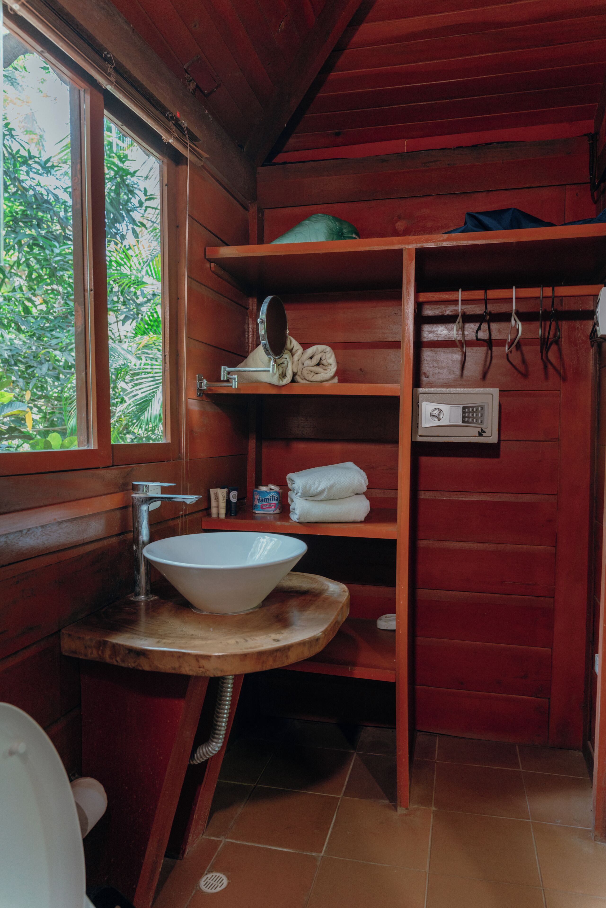 A wooden cabin bathroom with a sink, mirror, shelves, and a window.