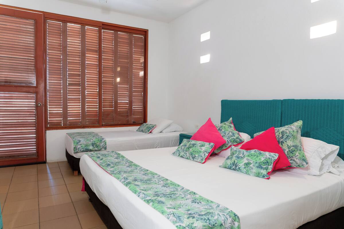 A hotel room with a large wooden door, two single beds, a double bed, and a teal headboard.