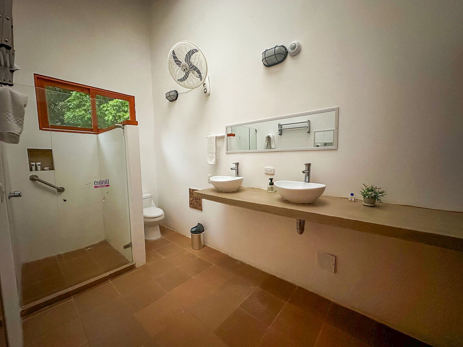 A bathroom with two sinks, a mirror, a fan, and a toilet.