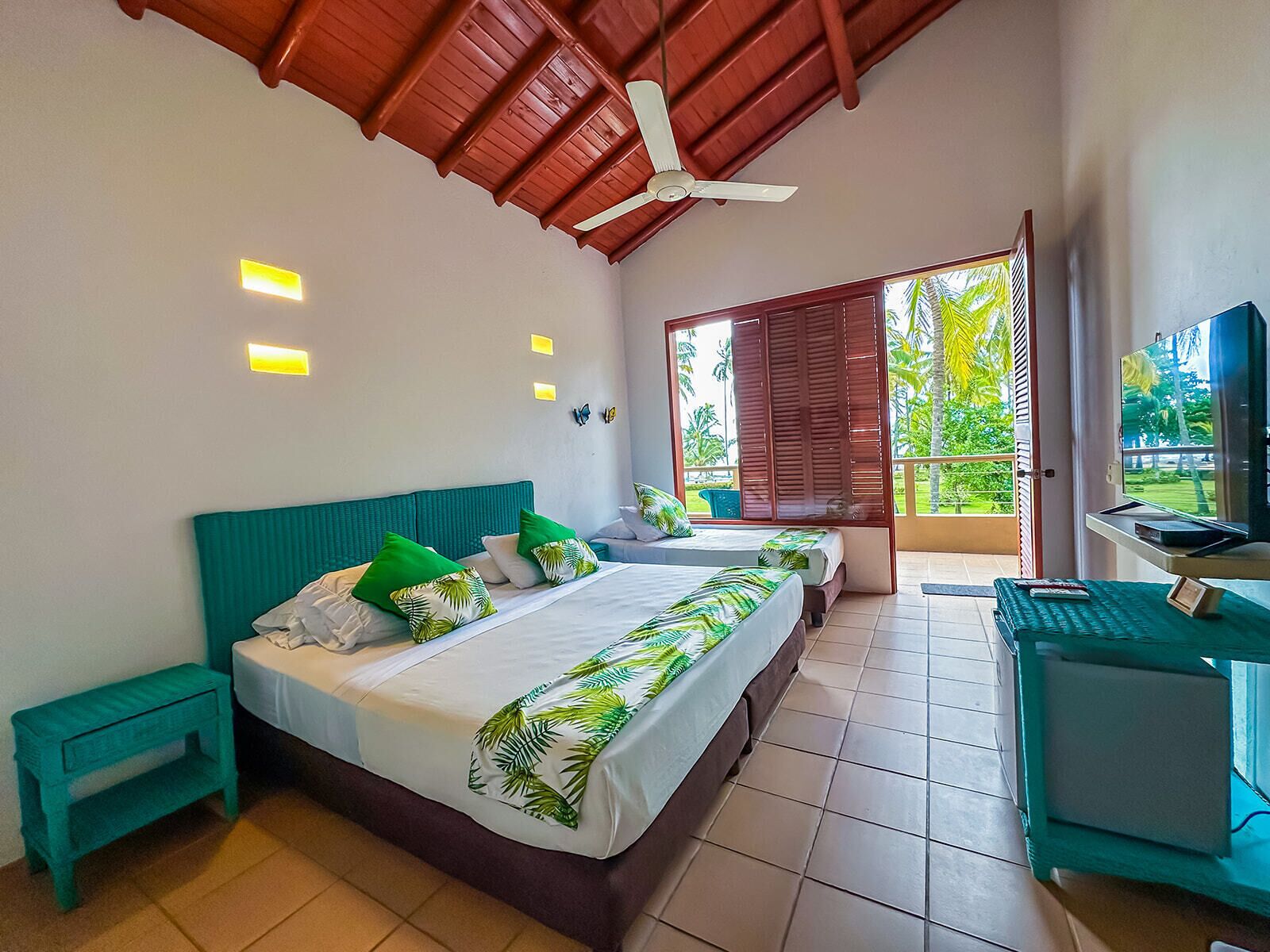Une chambre à coucher avec un lit, un bureau avec un ordinateur, un ventilateur de plafond et une vue sur l’extérieur.