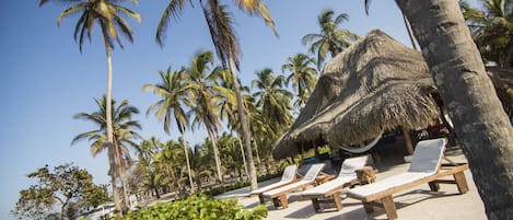 Un resort frente a la playa con cabañas de techo de paja, sillas de descanso y palmeras.