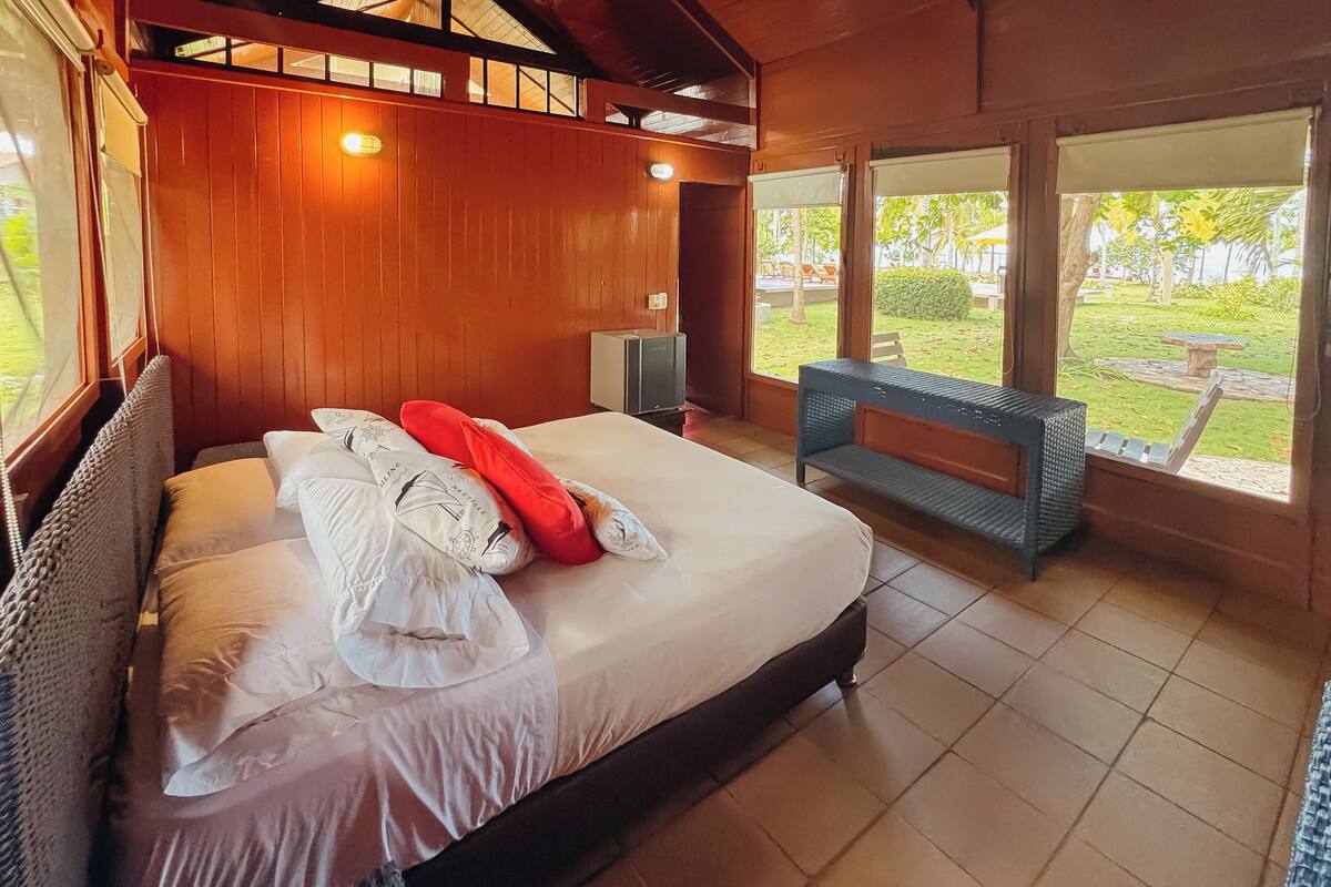 A bedroom with a bed, a bench, and a view of the garden.