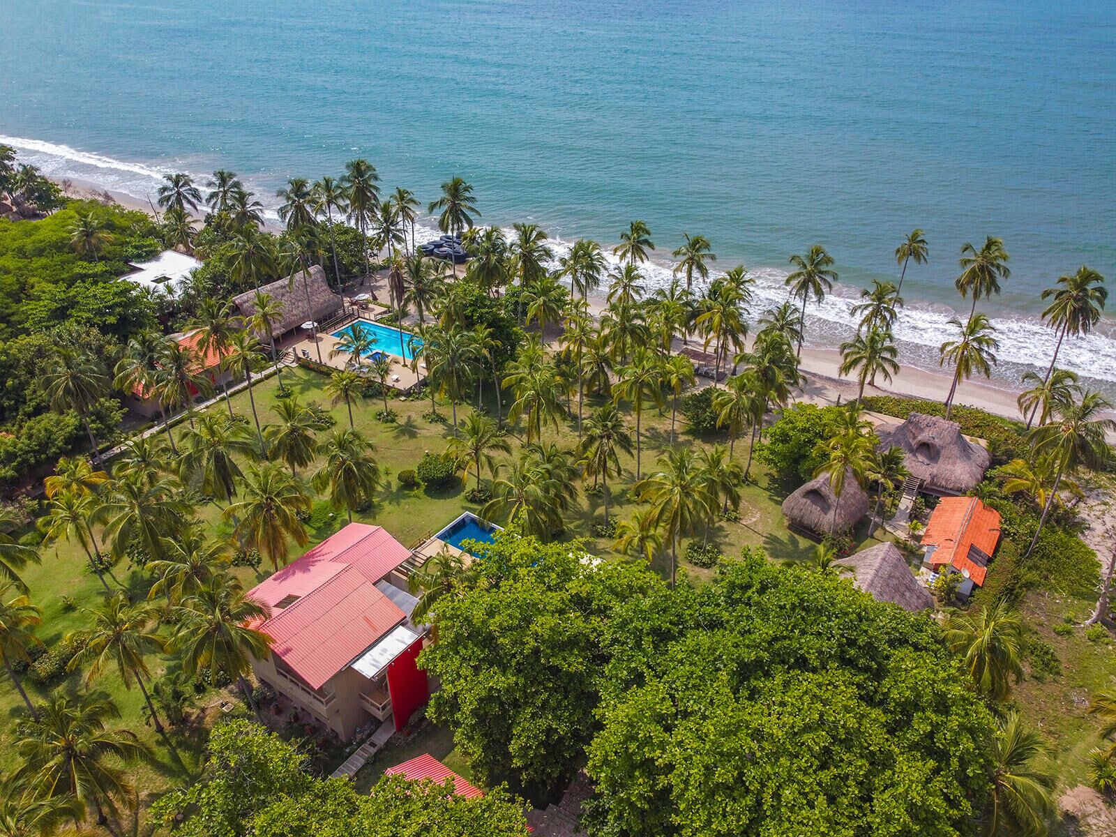 Een luchtbeeld van een resort met een zwembad, strand en palmbomen.