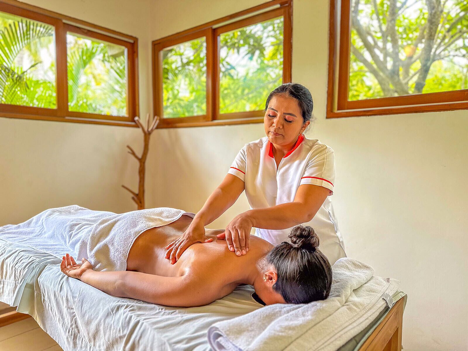 A massage therapy session in a room with large windows and a view of greenery.
