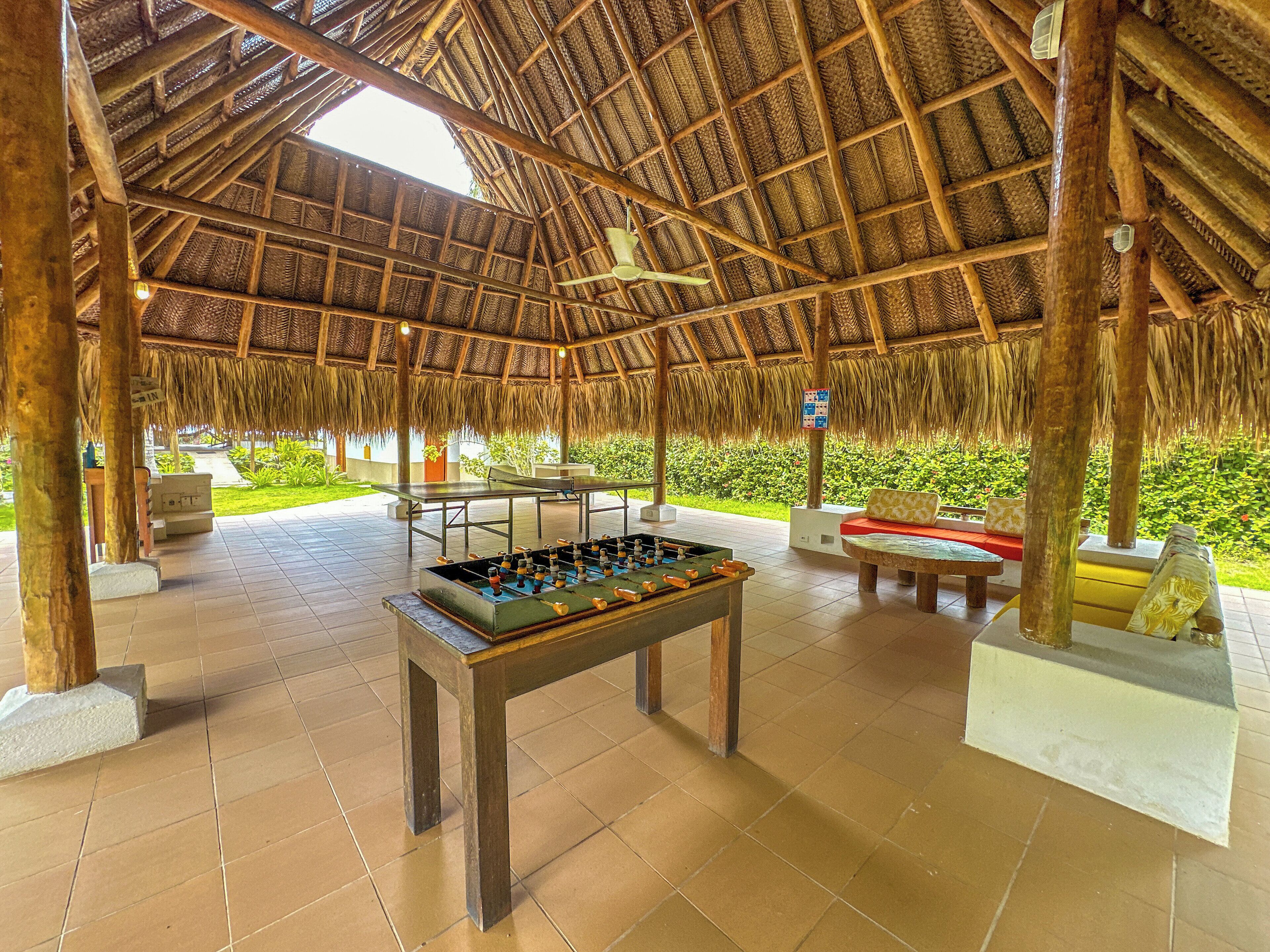 An indoor recreational area with a foosball table, seating, and a thatched roof structure.